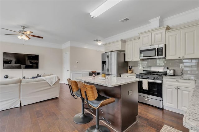 kitchen with dark wood-style floors, a center island, stainless steel appliances, visible vents, and a kitchen bar