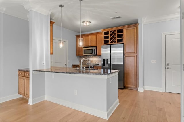 kitchen featuring brown cabinets, dark stone countertops, stainless steel appliances, light wood-style floors, and backsplash