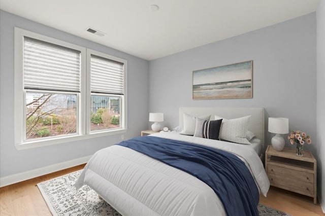 bedroom with baseboards, visible vents, and wood finished floors