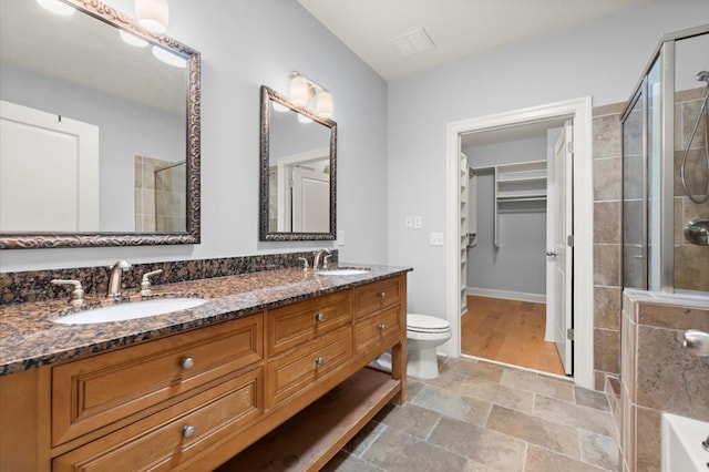 full bath featuring a tile shower, double vanity, a sink, and a walk in closet