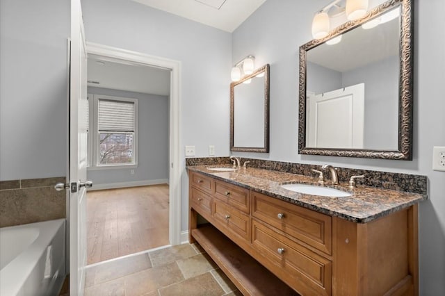 full bath featuring double vanity, baseboards, a bathtub, and a sink