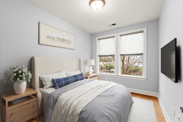 bedroom with wood finished floors, visible vents, and baseboards