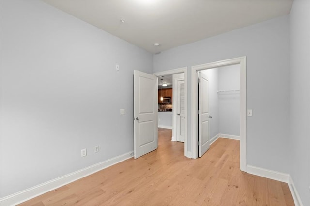 unfurnished bedroom featuring light wood-type flooring, a spacious closet, baseboards, and a closet