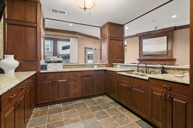 kitchen with tasteful backsplash, visible vents, light stone counters, crown molding, and a sink