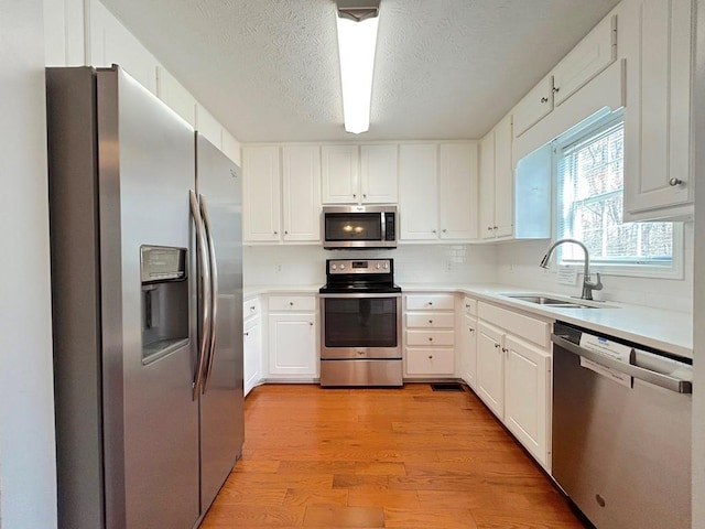 kitchen featuring light countertops, light wood-style floors, white cabinets, stainless steel appliances, and a sink