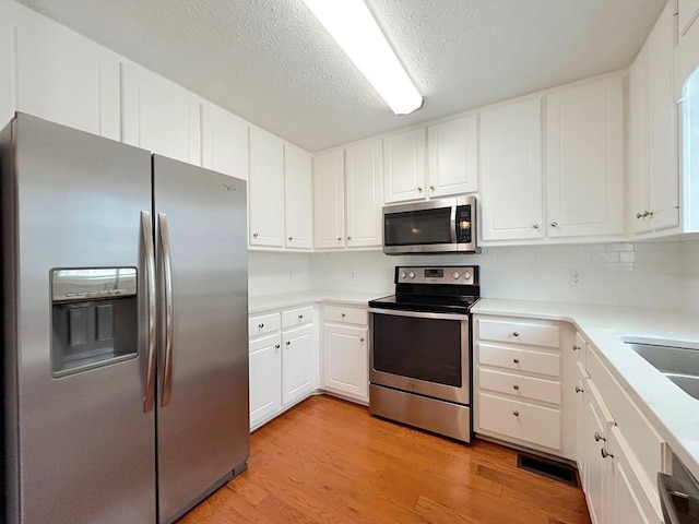 kitchen featuring light wood-style floors, appliances with stainless steel finishes, white cabinets, light countertops, and decorative backsplash