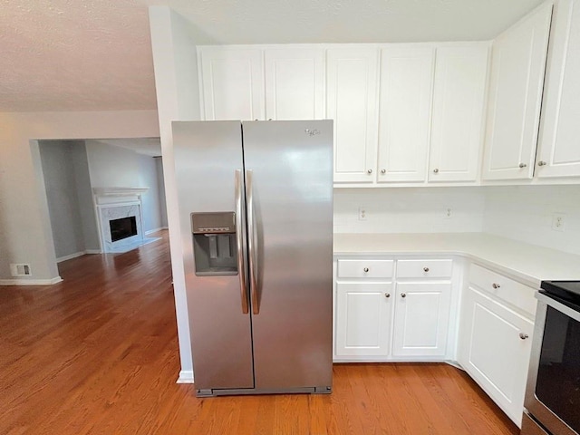 kitchen featuring visible vents, a premium fireplace, light wood-style flooring, light countertops, and stainless steel refrigerator with ice dispenser