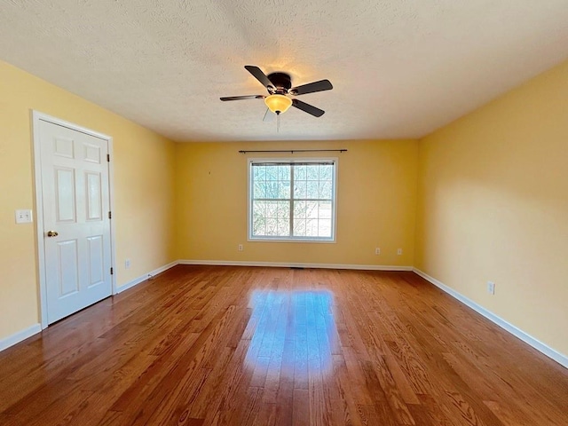 empty room featuring a textured ceiling, wood finished floors, baseboards, and ceiling fan