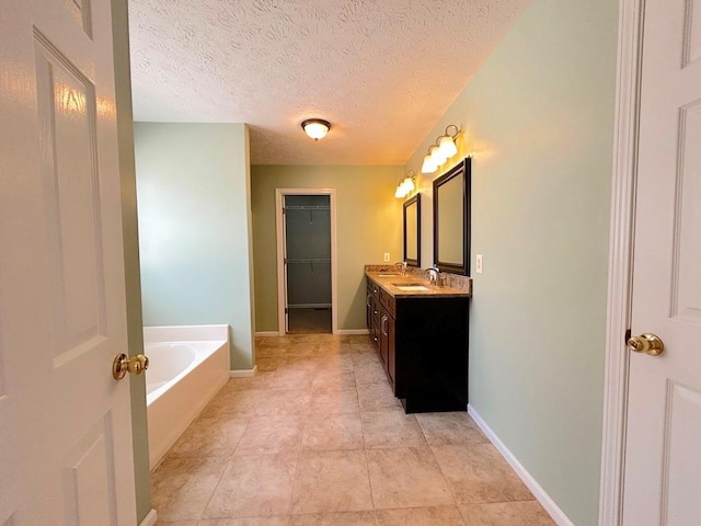 full bath featuring baseboards, a textured ceiling, a bath, and vanity