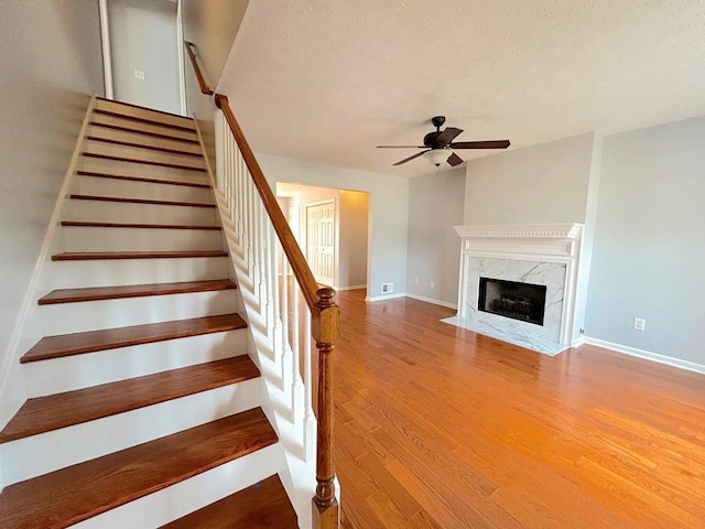 stairway with wood finished floors, a ceiling fan, baseboards, and a textured ceiling