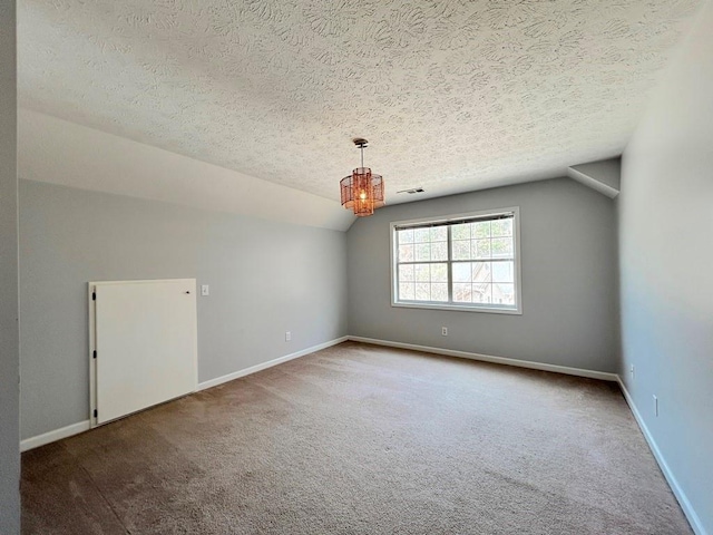 empty room with visible vents, a textured ceiling, carpet flooring, baseboards, and vaulted ceiling