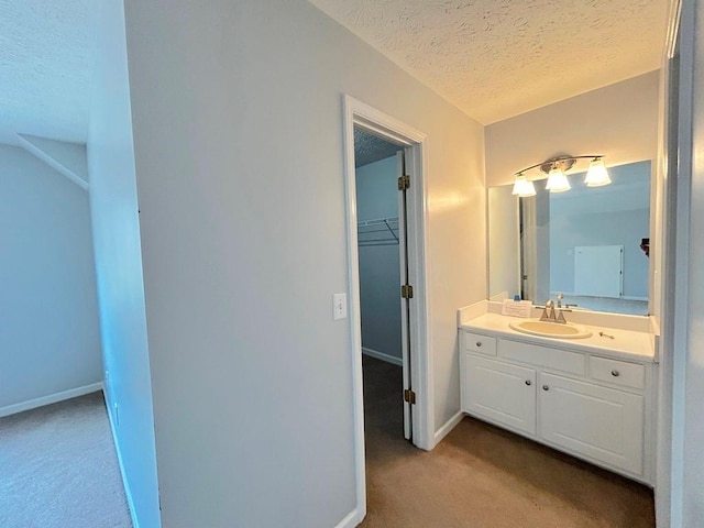 bathroom featuring a walk in closet, a textured ceiling, vanity, and baseboards