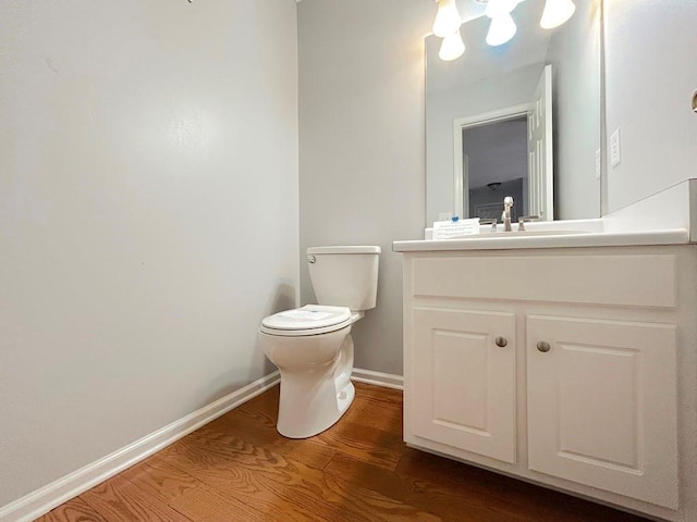 bathroom with vanity, toilet, wood finished floors, and baseboards