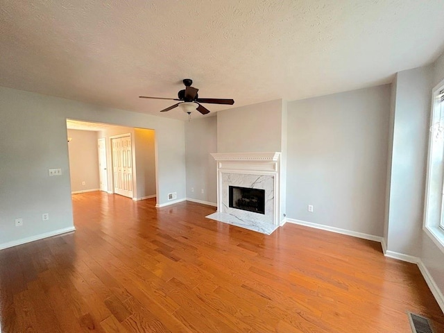 unfurnished living room featuring wood finished floors, baseboards, a ceiling fan, visible vents, and a premium fireplace