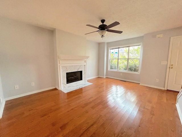 unfurnished living room featuring a high end fireplace, visible vents, baseboards, wood finished floors, and a ceiling fan