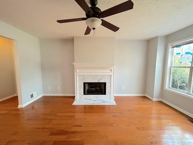 unfurnished living room featuring a premium fireplace, visible vents, baseboards, and wood finished floors