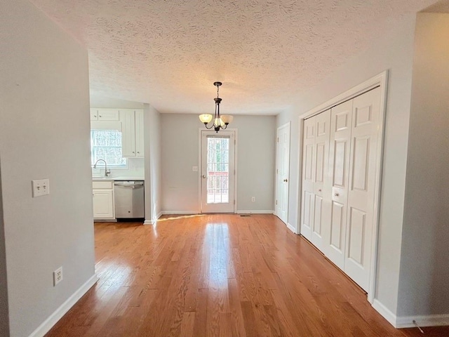 unfurnished dining area with an inviting chandelier, light wood-style floors, baseboards, and a sink