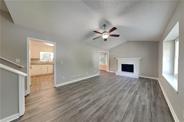 1011 Darvin Ln NW, Kennesaw, GA 30144 - unfurnished living room featuring a ceiling fan, lofted ceiling, light wood finished floors, plenty of natural light, and a brick fireplace