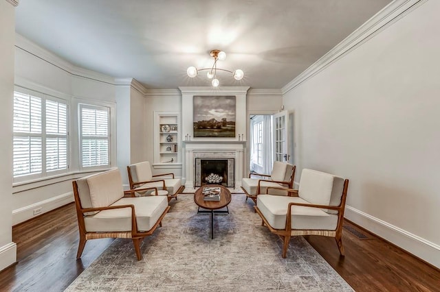 sitting room with a notable chandelier, hardwood / wood-style flooring, ornamental molding, and built in shelves