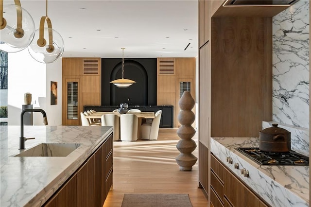 kitchen with decorative light fixtures, sink, stainless steel gas cooktop, light stone counters, and light hardwood / wood-style flooring