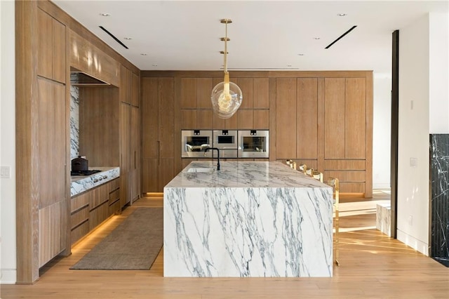 kitchen with pendant lighting, sink, light hardwood / wood-style floors, light stone counters, and a spacious island