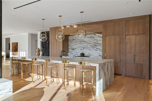 bar with pendant lighting, light hardwood / wood-style flooring, light stone countertops, and tasteful backsplash