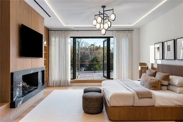 bedroom with a raised ceiling, a chandelier, a fireplace, and light hardwood / wood-style flooring