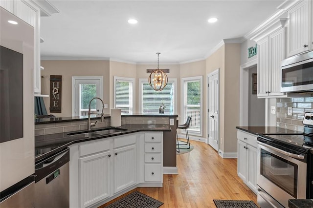 kitchen with white cabinets, light wood finished floors, a sink, a notable chandelier, and appliances with stainless steel finishes