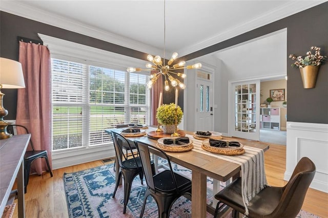 dining space with light wood-style floors, a notable chandelier, ornamental molding, and visible vents