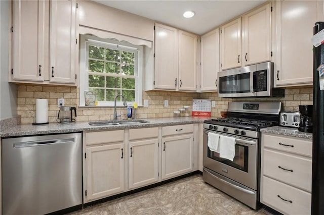 kitchen with stainless steel appliances, tasteful backsplash, light stone countertops, sink, and light tile floors