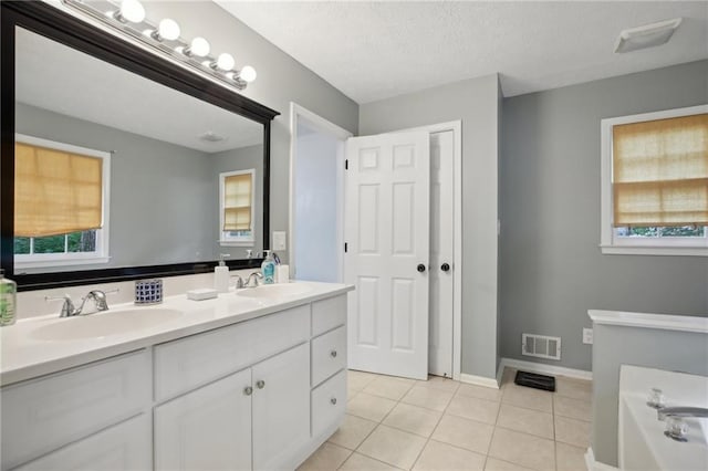 bathroom with a textured ceiling, double sink, a bath to relax in, tile floors, and oversized vanity