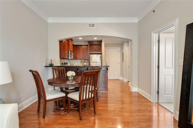 dining room with ornamental molding, arched walkways, light wood-style floors, and baseboards