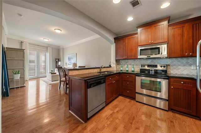 kitchen with stainless steel appliances, dark countertops, crown molding, decorative backsplash, and a peninsula
