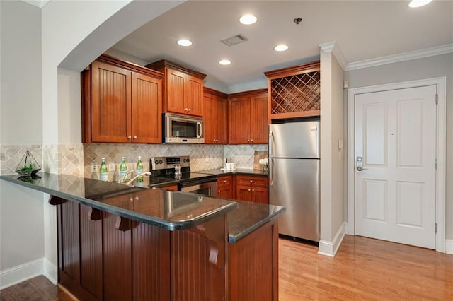 kitchen with stainless steel appliances, a peninsula, brown cabinets, arched walkways, and light wood-style flooring