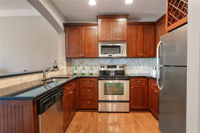 kitchen featuring appliances with stainless steel finishes, a sink, a peninsula, light wood-type flooring, and tasteful backsplash