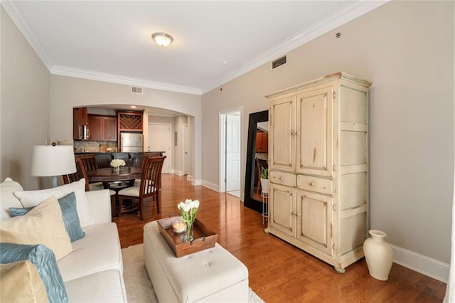 living room with arched walkways, ornamental molding, baseboards, and light wood-type flooring