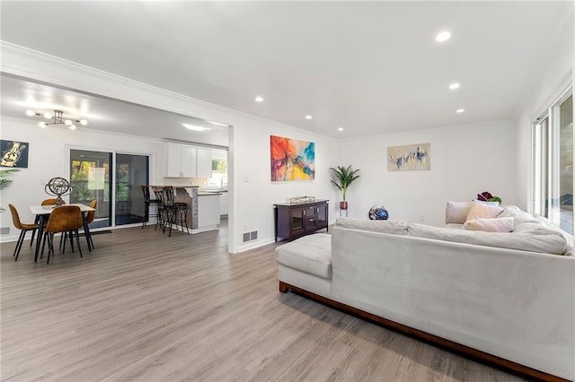 living room with light hardwood / wood-style floors, an inviting chandelier, and crown molding