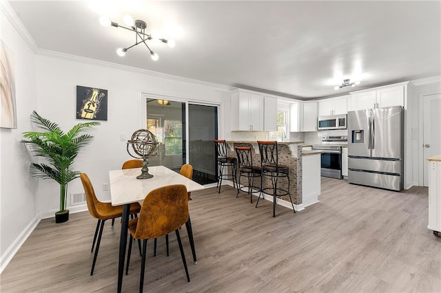 dining space featuring an inviting chandelier, ornamental molding, sink, and light hardwood / wood-style flooring