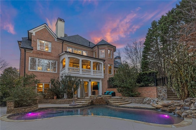 back house at dusk featuring pool water feature, a balcony, and ceiling fan