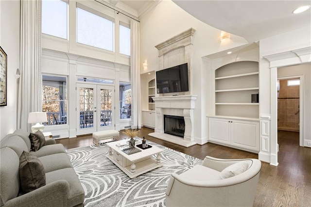 living room featuring dark wood-type flooring, a tile fireplace, french doors, built in shelves, and a towering ceiling