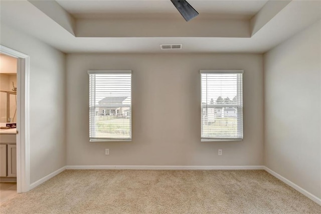 empty room featuring a tray ceiling, baseboards, light colored carpet, and visible vents