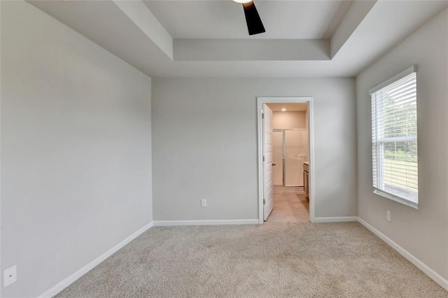 spare room featuring light colored carpet, baseboards, a tray ceiling, and ceiling fan