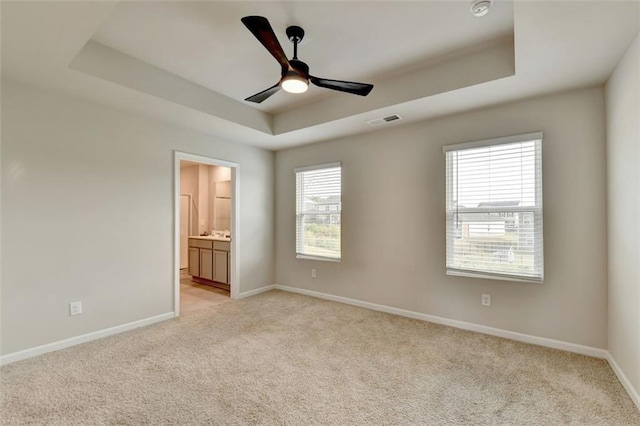 empty room featuring visible vents, light colored carpet, baseboards, and a tray ceiling