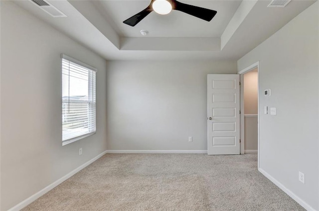 empty room with visible vents, ceiling fan, baseboards, carpet, and a tray ceiling