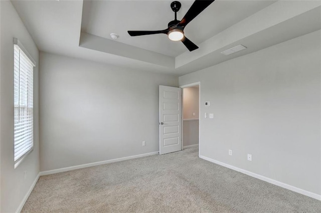 carpeted empty room featuring baseboards, a raised ceiling, and plenty of natural light