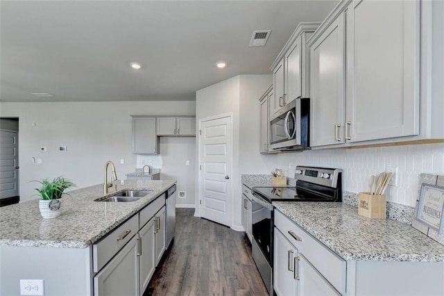 kitchen featuring visible vents, a sink, stainless steel appliances, light stone countertops, and dark wood-style flooring