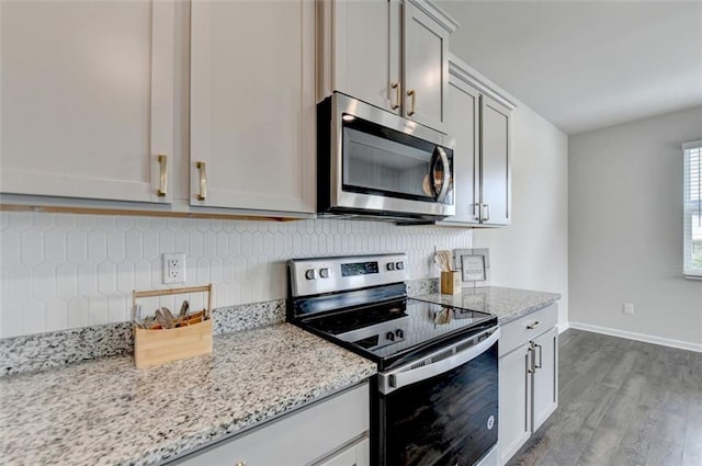 kitchen featuring light stone countertops, wood finished floors, baseboards, appliances with stainless steel finishes, and backsplash