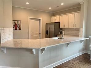 kitchen with kitchen peninsula, white cabinets, a kitchen bar, and stainless steel fridge with ice dispenser