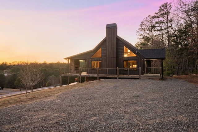 back of house at dusk with a deck and a chimney