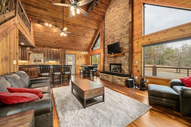 living room featuring ceiling fan, wood walls, hardwood / wood-style floors, a fireplace, and wooden ceiling